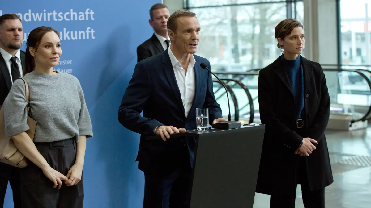 Wirtschafts- und Umweltminister Bauer (Mitte, Hannes Jaenicke) hält eine umstrittene Rede, seine Personenschützerin Helen Schilling (r., Svenja Jung) und Staatssekretärin Dr. Karlström (l.,Mina Tander) sind über die Reaktionen des Publikums besorgt.