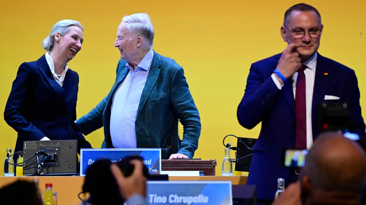GERMANY-POLITICS-PARTIES-FAR RIGHT-AFD: AfD co-leaders Tino Chrupalla (R) and Alice Weidel (L) and honorary chairman Alexander Gauland greet delegates at the party congress of far-right Alternative for Germany (AfD) at the Messe Erfurt fairground in Erfurt, eastern Germany on July 4, 2026. Thousands of demonstrators flooded a German city on July 4, blocking major roads and disrupting public transport, in a bid to shut down the annual congress of the far-right AfD party. About 20,000 people flocked to Erfurt, in Thuringia state, according to police, to protest against the Alternative for Germany (AfD) party that tops national opinion polls. (Photo by John MACDOUGALL / AFP)