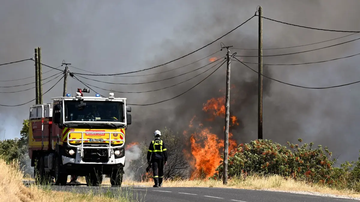Waldbrände in Südfrankreich: 05.07.2026, Frankreich, Ille-sur-Têt: Ein Feuerwehrmann der französischen Zivilschutzbehörde geht auf einer Straße neben einem Waldbrand in der Nähe von Ille-sur-Têt. Ein Waldbrand war am 4. Juli in einem schwer zugänglichen Gebirgsmassiv in der Nähe von Trevillach ausgebrochen. Foto: Matthieu Rondel/AFP/dpa +++ dpa-Bildfunk +++