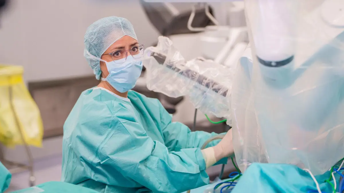 Klinikum Darmstadt: PRODUKTION - 26.06.2026, Hessen, Darmstadt: Chirurgin Florentine Hüttl sitzt im Zentral-OP am Operationstisch und assistiert dem Operateur bei einem Eingriff im Bauchbereich mit dem Operationsroboter "DAVINCI". Das Da-Vinci-Operationssystem ist eines der weltweit modernsten roboterassistierten Systeme für minimalinvasive Eingriffe; der Chirurg respektive die Chirurgin operiert nicht selbstständig, sondern steuert die präzisen Roboterarme von einer Konsole aus, während er das Operationsgebiet in dreidimensionaler Full-HD-Sicht sieht. (zu dpa: «Frauen in der Chirurgie: Karriere mit Messer und Mut») Foto: Andreas Arnold/dpa +++ dpa-Bildfunk +++