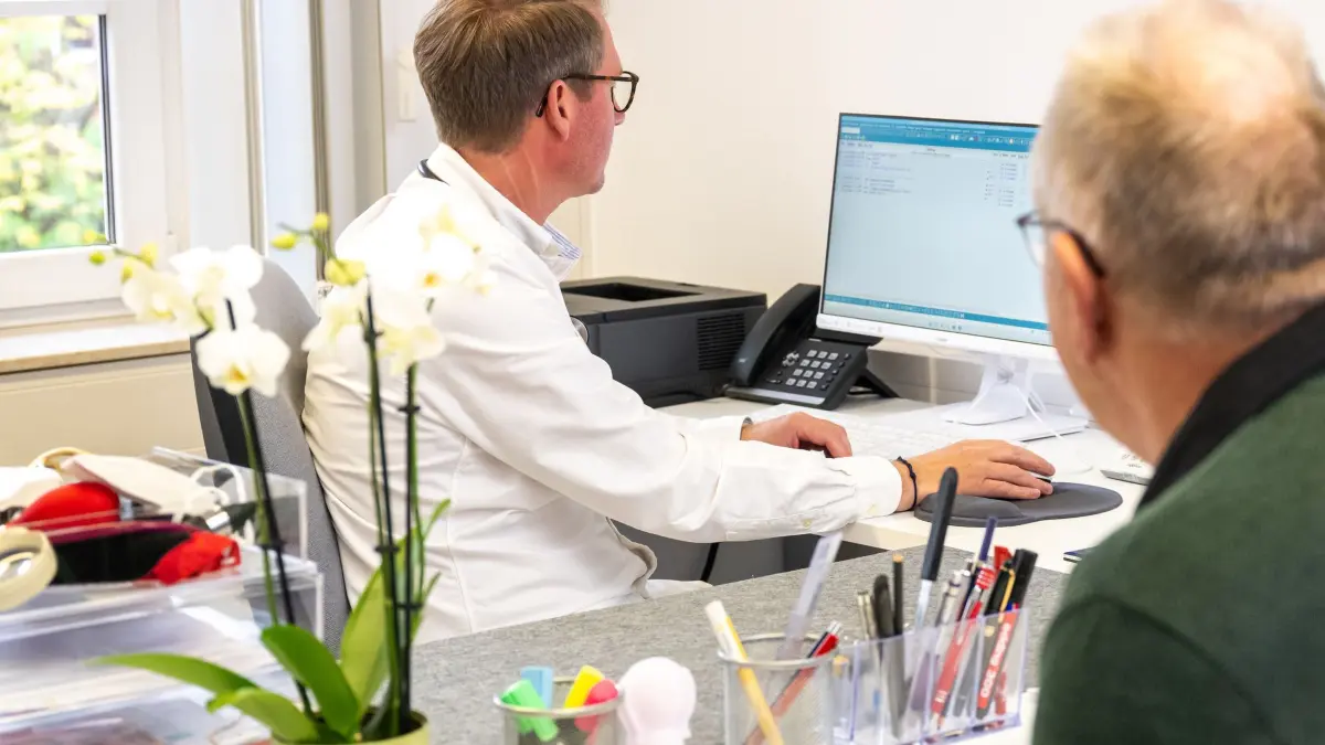 Ein Arzt schaut vor einem Patieten in einen Computer: ILLUSTRATION - Bald mehr Einblick für den Betriebsarzt? Ein Referentenentwurf sieht vor, dass Betriebsärzte künftig auf die elektronische Patientenakte zugreifen können – Beschäftigte müssten aktiv widersprechen. (zu dpa: «E-Akte für Betriebsärzte: Patienten können Zugang sperren») Foto: Benjamin Nolte/dpa-mag - Honorarfrei nur für Bezieher des Dienstes dpa-Magazin +++ dpa-Magazin +++