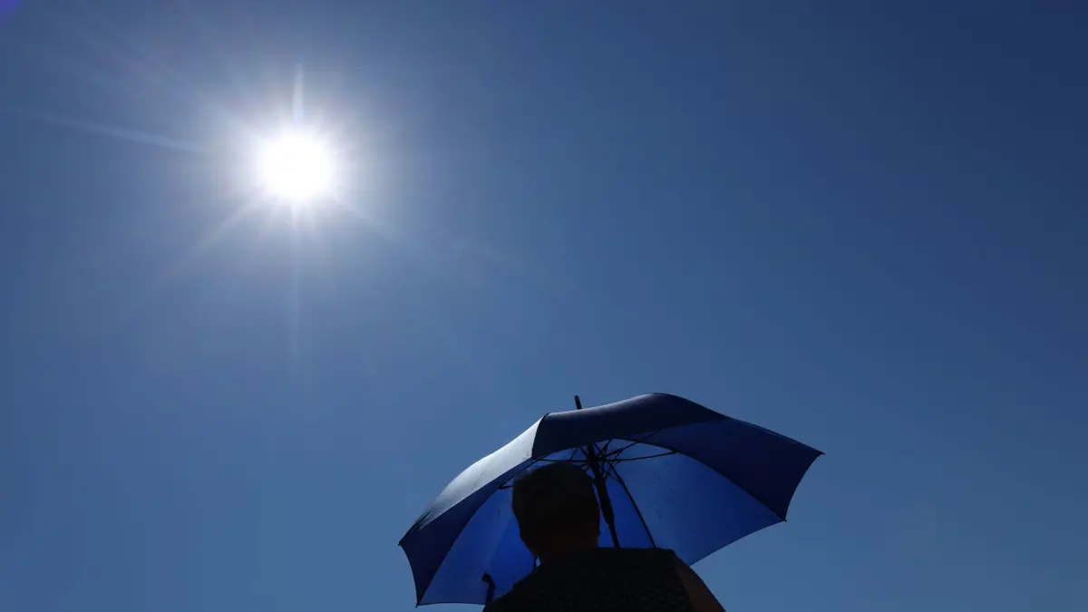 Wetter in Bayern: 11.07.2026, Bayern, Marktoberdorf: Eine Frau läuft mit Sonnenschirm unter der strahlenden Sonne. Foto: Karl-Josef Hildenbrand/dpa +++ dpa-Bildfunk +++