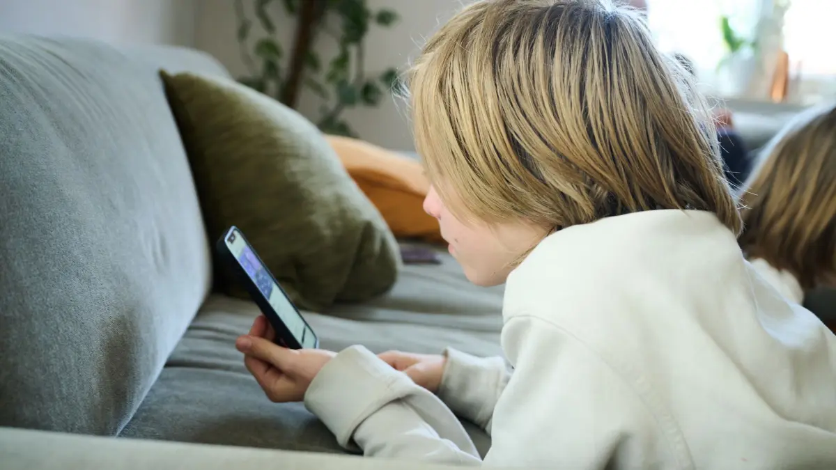 Handynutzung Kinder: ARCHIV - 21.04.2025, Bayern, Roth: ILLUSTRATION - Ein Junge liegt auf einem Sofa und guckt auf sein Smartphone. (gestellte Szene) (zu dpa: «Social-Media-Mindestalter? EU-Experten geben Empfehlung ab») Foto: Annette Riedl/dpa +++ dpa-Bildfunk +++