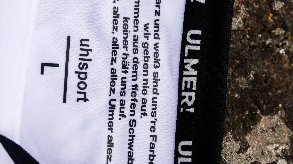 15.07.2026, Fussball, Saison 2026/2027, Regionalliga Südwest, Fischerviertel Ulm, Shooting Produktbilder Vorstellung Heimtrikot weiß der Saison 2026-2027: 15.07.2026, Fussball, Saison 2026/2027, Regionalliga Südwest, Fischerviertel Ulm, Shooting Produktbilder Vorstellung Heimtrikot weiß der Saison 2026-2027 Detailaufnahme Kragen innenseite mit dem Fangesang „Schwarz und weiß sind unsre Farben“ .. „Wir geben nie auf!“
Foto:Eibner-Pressefoto/Lucca Fundel