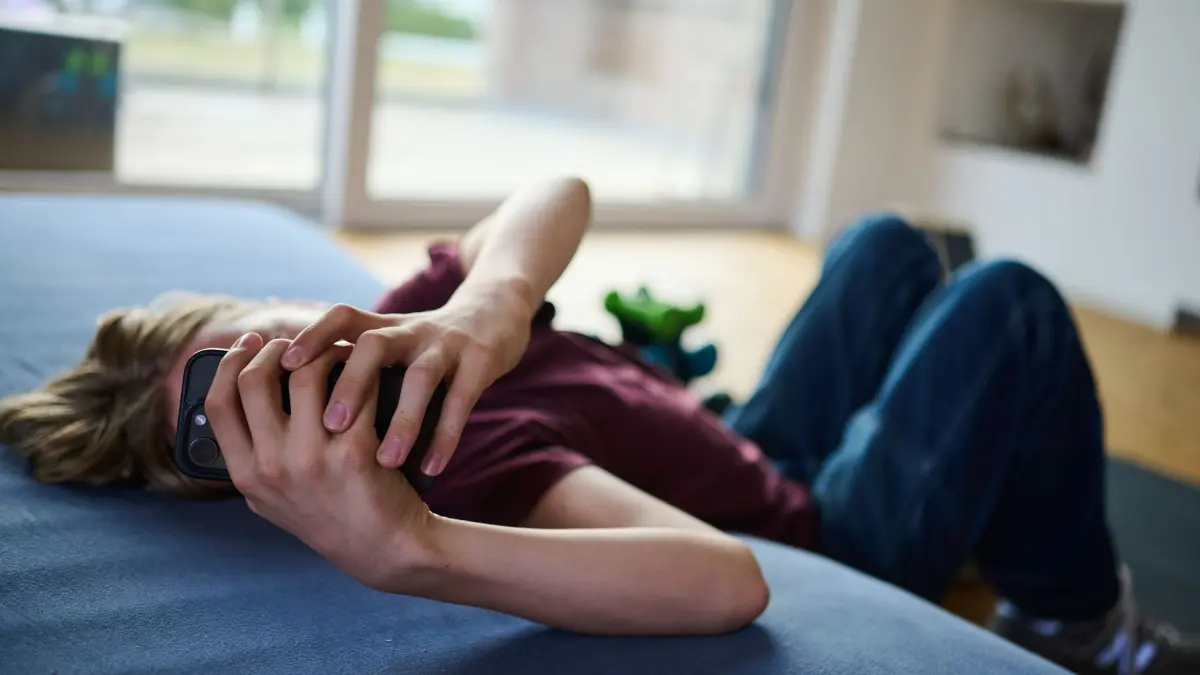 Illustration - Jugendliche und Social media: ILLUSTRATION - 10.07.2026, Brandenburg, Königs Wusterhausen: Ein Teenager guckt auf ein Handy, während er auf Boden und Matratze liegt. (gestellte Szene)
Fachleute raten zu einer Altersgrenze, wenn es um TikTok, Snapchat und Insta geht. (zu dpa: «Studie: Jugendliche erleben Social Media als Achterbahnfahrt») Foto: Annette Riedl/dpa +++ dpa-Bildfunk +++