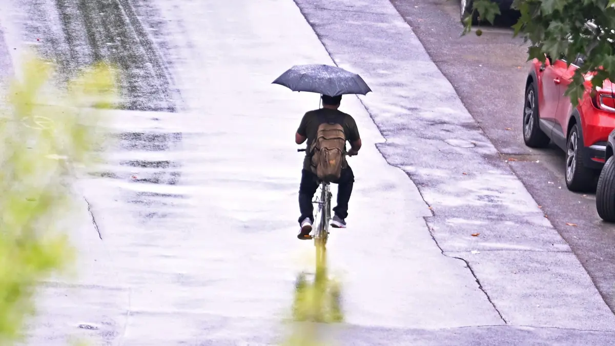 Regenwetter im Rhein-Main-Gebiet: 17.07.2026, Hessen, Offenbach am Main: Ein Fahrradfahrer fährt mit einem Regenschirm in der Hand über eine regennasse Straße. Nach Angaben des Deutschen Wetterdienstes besteht bereits am Vormittag in Hessen ein zunehmendes Gewitterrisiko. Im Tagesverlauf sind verbreitet Schauer und Gewitter mit Starkregen, Hagel und Sturmböen möglich. Foto: Jennifer Brückner/dpa +++ dpa-Bildfunk +++