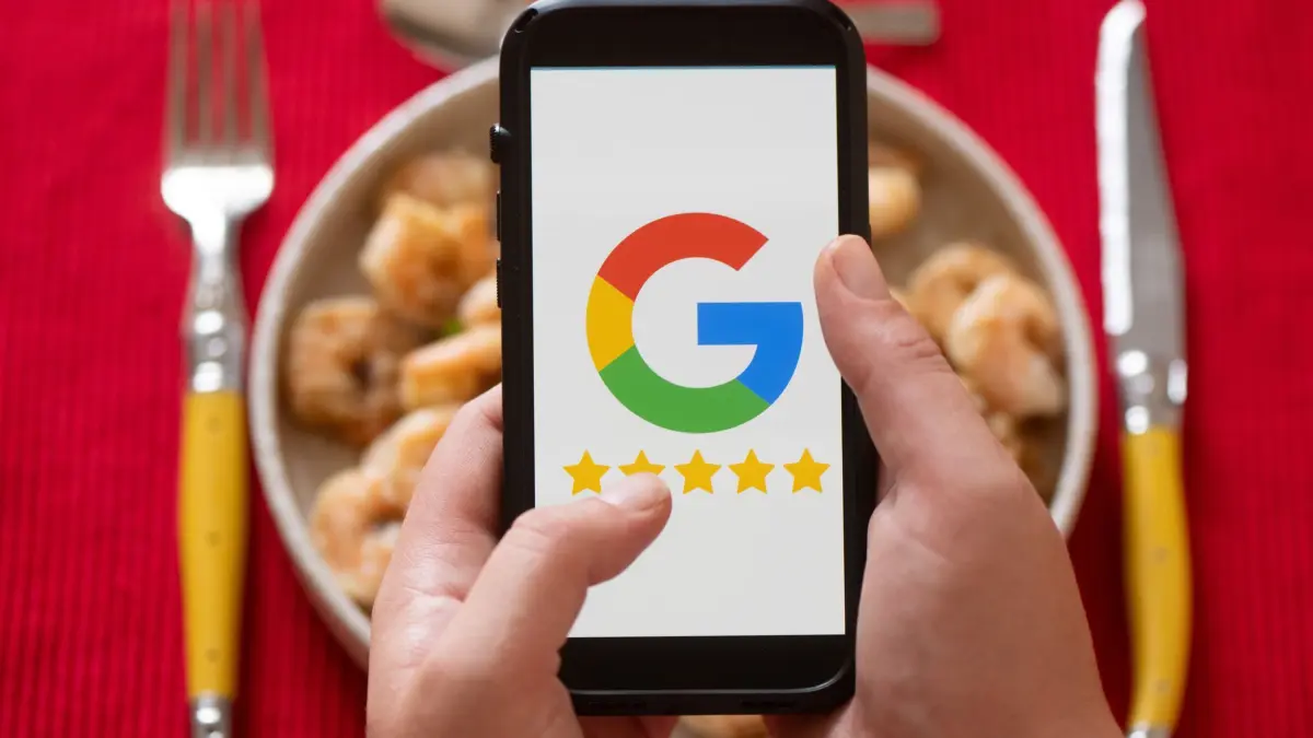 Google-Rezensionen: 17.07.2026, Sachsen, Dresden: Eine Frau hält vor einem gedeckten Esstisch ein Smartphone mit dem Google-Logo. Foto: Sebastian Kahnert/dpa +++ dpa-Bildfunk +++