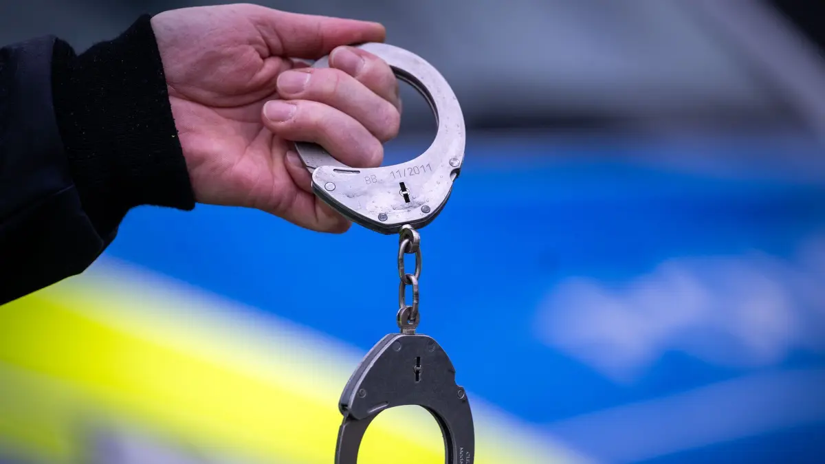 Festnahme (Symbolbild): ARCHIV - 22.03.2024, Brandenburg, Trebbin: Ein Polizist hält ein Paar Handschellen. (zu dpa: «Messerangriff auf ehemalige Partnerin des Sohnes») Foto: Soeren Stache/dpa +++ dpa-Bildfunk +++