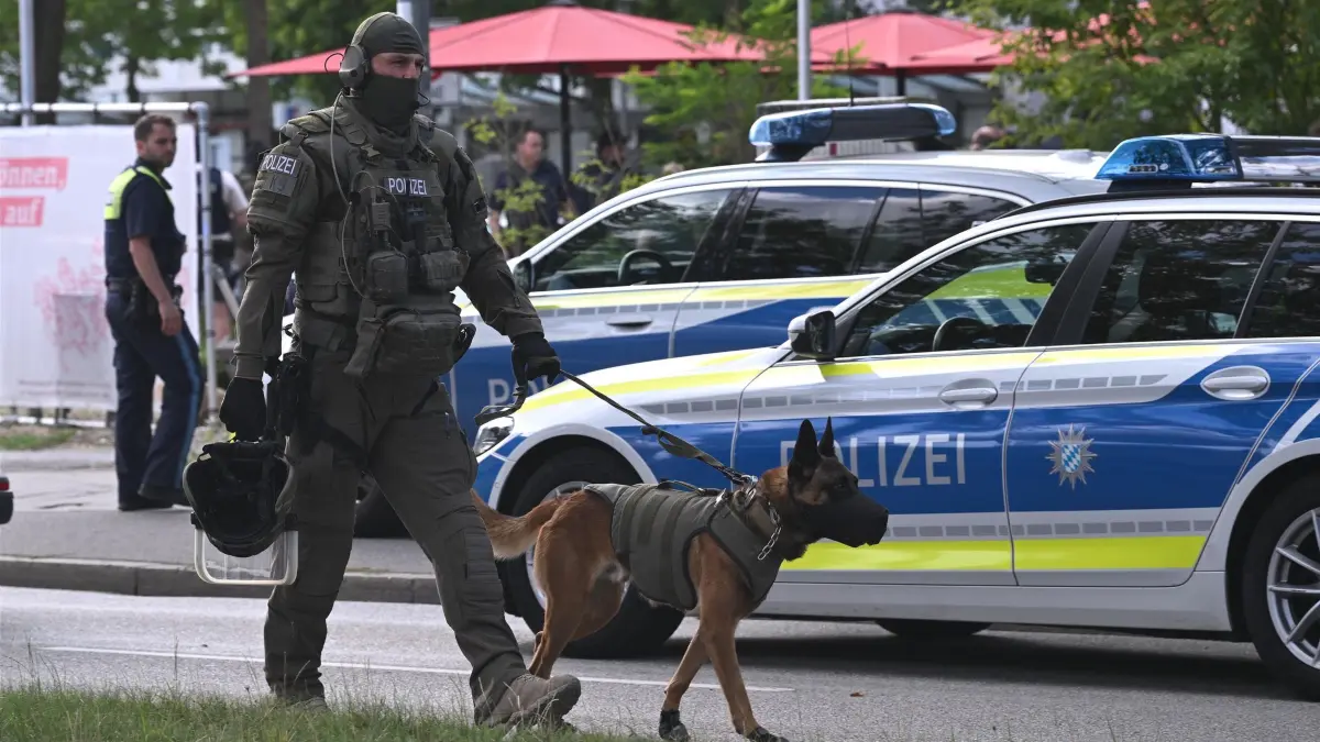 Attacke in Bank in Regensburg: 23.07.2026, Bayern, Regensburg: Ein Polizist ist mit einem Diensthund im Einsatz. Bei einem Messerangriff in einer Bankfiliale in Regensburg ist ein Mann ums Leben gekommen. Zunächst hatte die Polizei von einer Geiselnahme in der Bank gesprochen. Foto: Jason Tschepljakow/dpa +++ dpa-Bildfunk +++