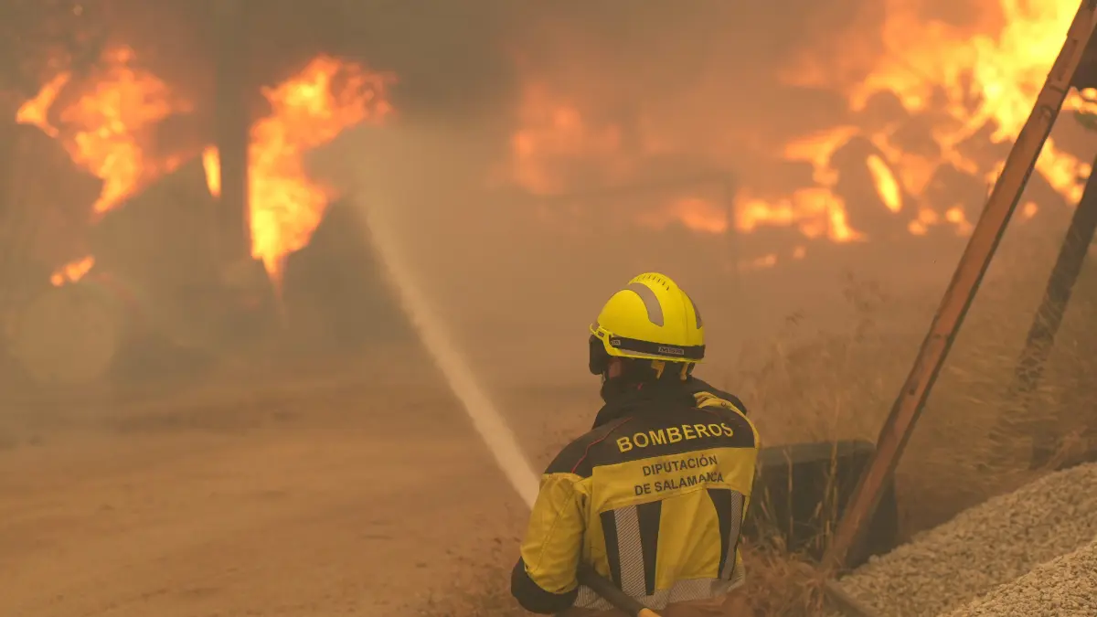 SPAIN-WILDFIRE-EMERGENCY-GOVERNMENT-CLIMATE: A firefighter waters burning tires and barrels while battling a wildfire in Cebreros area, near Avila, 80 kms west of Madrid on July 24, 2026. The worst wildfires in the Madrid region's history rage west of the Spanish capital, forcing authorities to evacuate or order around 40,000 people to remain indoors. (Photo by Cesar MANSO / AFP)