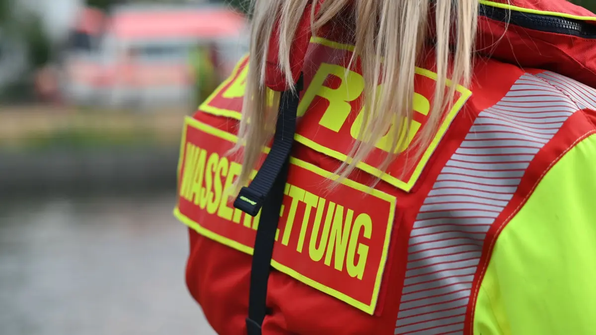 DLRG-Übung in Baden-Württemberg: PRODUKTION - 29.06.2026, Baden-Württemberg, Remseck: Ein Mitglied der Deutschen Lebens-Rettungs-Gesellschaft (DLRG) blickt bei einer Rettungsübung auf dem Neckar von einem Boot aus auf das Festland, wo ein Rettungswagen steht. (zu dpa: «Not im Nichtschwimmerbereich - Mann stirbt») Foto: Jennifer Kramer/dpa +++ dpa-Bildfunk +++