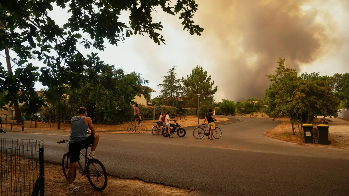 Menschen beobachten die Rauchwolken von Waldbränden: Feuer im Anmarsch in der Gironde und les Landes: Damit man nicht überrascht wird, rät das Auswärtige Amt, die lokalen Warneinrichtungen zu nutzen. (zu dpa: «Waldbrände: Aktuelle Informationen für Urlauber») Foto: Caroline Blumberg/AP/dpa-tmn - ACHTUNG: Nur zur redaktionellen Verwendung im Zusammenhang mit dem genannten Text - Honorarfrei nur für Bezieher des dpa-Themendienstes +++ dpa-Themendienst +++