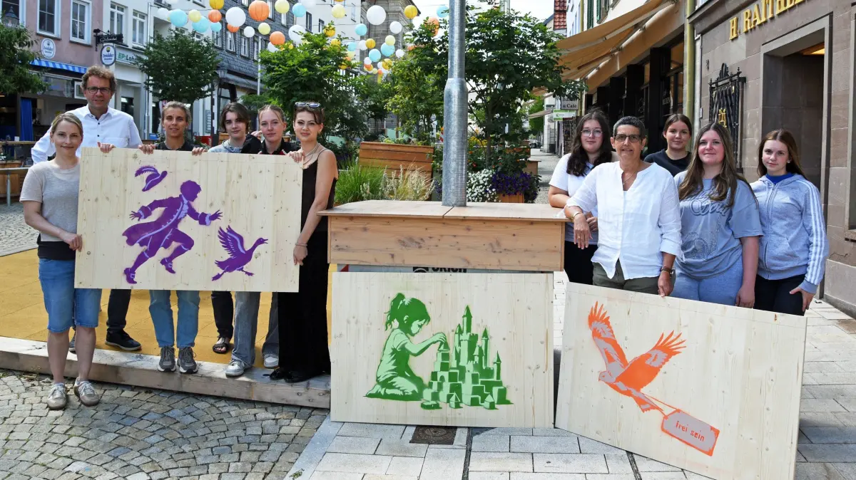 Bei der Vorstellung der Ergebnisse des Kunstprojekts auf dem Hechinger Marktplatz (von links): Kunstlehrerin Mirka Schorneck, der städtische Bautätigkeitsleiter Michael Werner, Stadtplanerin Patricia Krempels Uribe, dann die Schülerinnen mit der Ersten Beigeordneten Dorothee Müllges (4. v. r.). Die Motive zeigen von links die Gansfußsage aus dem Umfeld des Kinderfestes, die Burg Hohenzollern und den Rotmilan, der oft über der Altstadt kreist.
