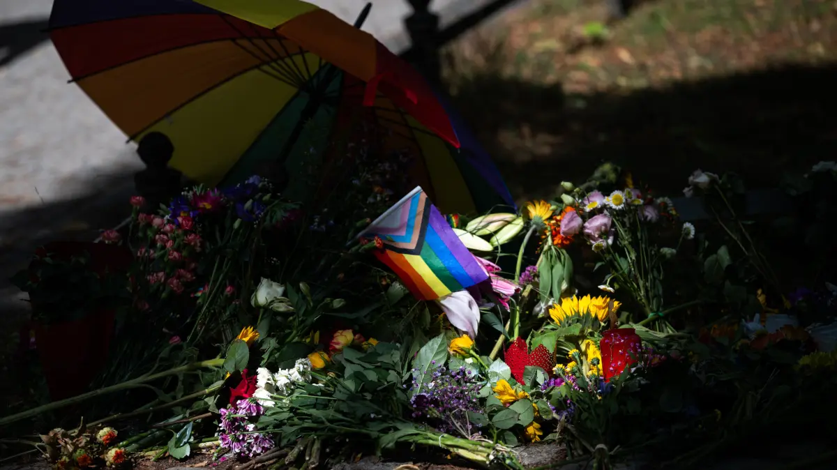 Die Sonne scheint auf Blumen und eine Progress-Pride-Fahne, die zum Gedenken an die Opfer des Anschlags auf den CSD abgelegt wurden. Im Tiergarten war am Rande des Christopher Street Day ein Mann mit einem Fahrzeug in eine Menschenmenge gefahren.