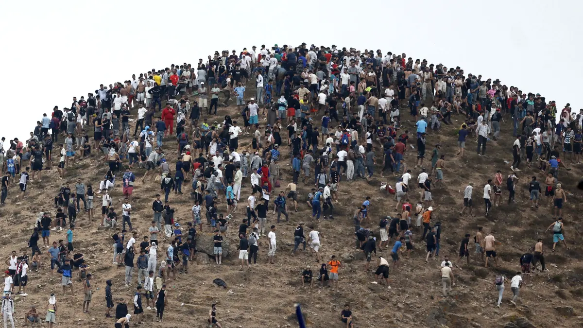 MOROCCO-SPAIN-MIGRATION: People gather on a hilltop close to the site of clashes near Fnideq, on the Morocco-Spain border, on July 31, 2026. Thousands of migrants crossed overnight from Morocco into Spain's north Africa's Ceuta enclave, a police source said on July 31, adding that it was impossible to estimate how many people in total. A total of 18 people died while attempting to reach the Spanish enclave, the source said. (Photo by Abdel Majid BZIOUAT / AFP)