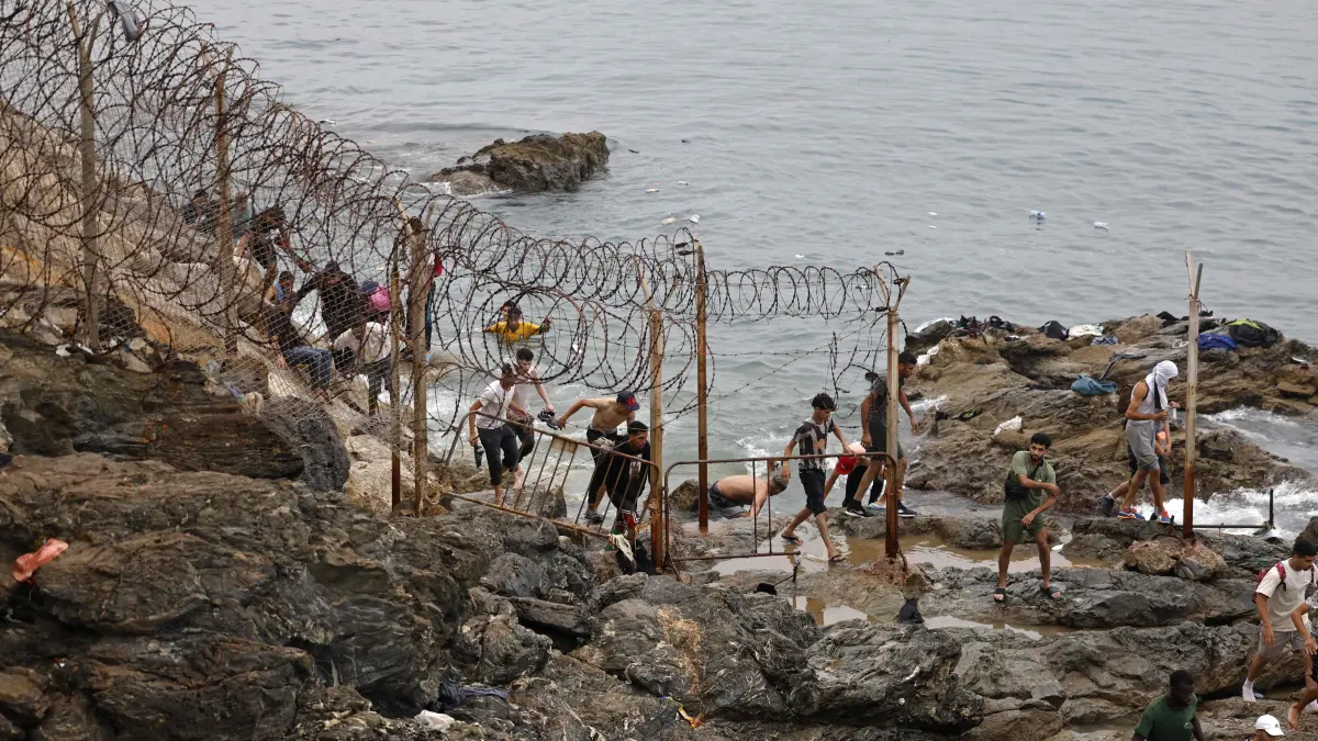MOROCCO-SPAIN-MIGRATION: People gather along the fence close to the site of clashes near Fnideq, on the Morocco-Spain border, on July 31, 2026. Thousands of migrants crossed overnight from Morocco into Spain's north Africa's Ceuta enclave, a police source said on July 31, adding that it was impossible to estimate how many people in total. A total of 18 people died while attempting to reach the Spanish enclave, the source said. (Photo by Abdel Majid BZIOUAT / AFP)