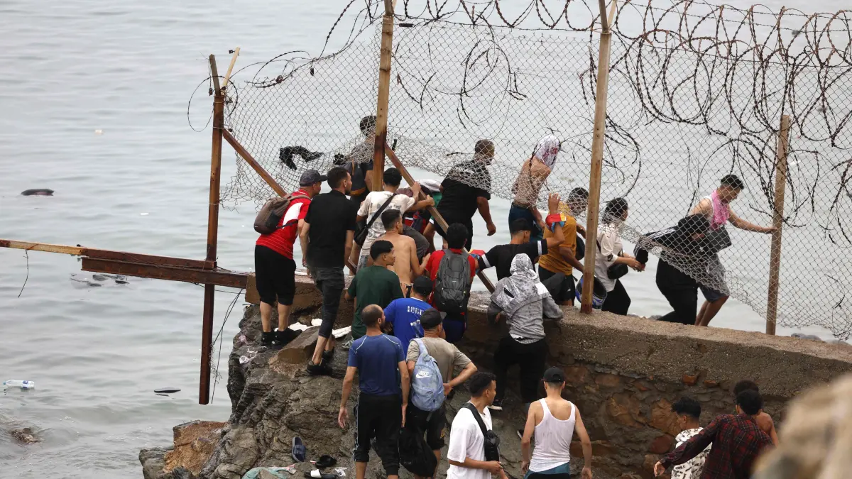 MOROCCO-SPAIN-MIGRATION: People gather along the fence close to the site of clashes near Fnideq, on the Morocco-Spain border, on July 31, 2026. Thousands of migrants crossed overnight from Morocco into Spain's north Africa's Ceuta enclave, a police source said on July 31, as Prime Minister Pedro Sanchez was set to arrive to manage the latest migrant crisis on the border. (Photo by Abdel Majid BZIOUAT / AFP)