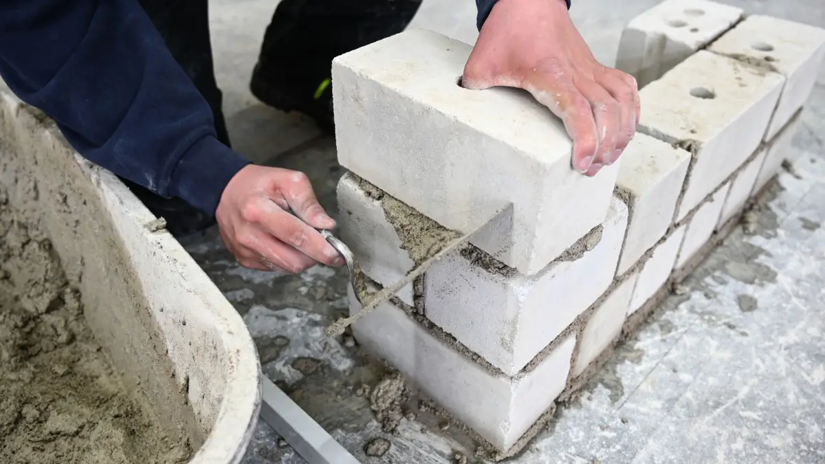 Ausbildung: ARCHIV - 14.03.2019, Baden-Württemberg, Ravensburg: Ein Auszubildender im Maurer-Handwerk nimmt in einem Ausbildungszentrum mit der Kelle den überstehenden Mörtel von der Mauer, die er im Unterricht gebaut hat. (zu dpa: «Vergütungen für Auszubildende steigen schneller als Löhne») Foto: Felix Kästle/dpa +++ dpa-Bildfunk +++