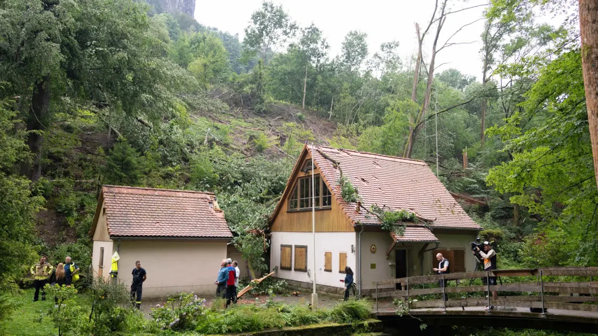Sturmschäden Sächsische Schweiz: 01.08.2026, Sachsen, Rathen: Sturmschäden an einem Gebäude der Bergwacht Sachsen im Amselgrund im Nationalpark Sächsische Schweiz. Nach dem schweren Unwetter mit einem Toten und drei Schwerverletzten ist der Nationalpark für Besucher gesperrt. Foto: Sebastian Kahnert/dpa +++ dpa-Bildfunk +++