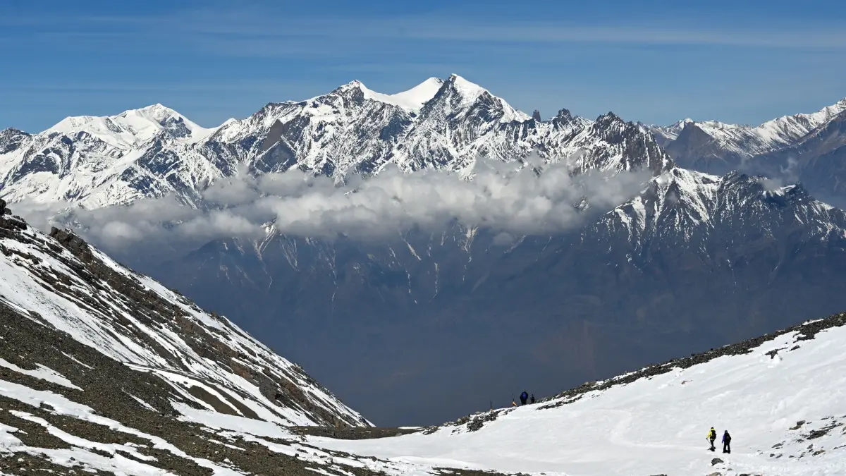 Himalaya Gebirge in Nepal: PRODUKTION - 17.04.2026, Nepal, Manang: Wanderer gehen am Thorong La Pass in der Annapurna-Region auf einem schneebedeckten Weg, im Hintergrund ragen schneebedeckte Berggipfel des Himalaya über einer Wolkenschicht auf. (zu dpa: «Fünf Leichen im Osten des Himalaya-Gebirges entdeckt») Foto: Elisa Schu/dpa +++ dpa-Bildfunk +++