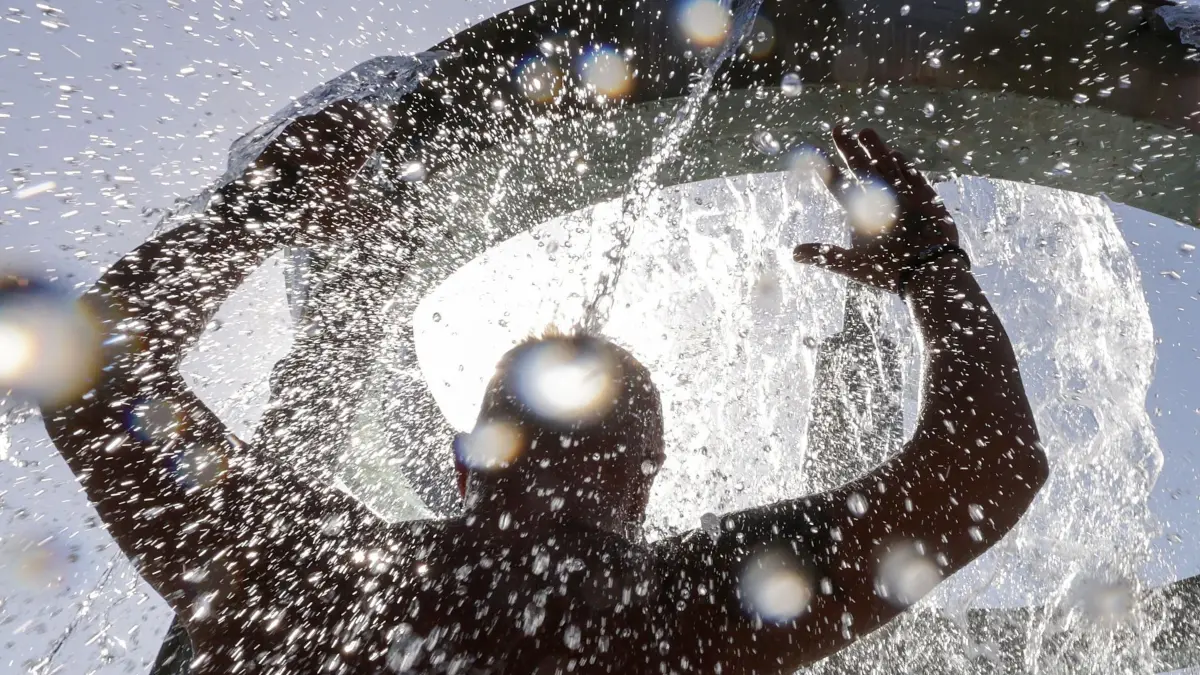 Wetter in Baden-Württemberg: 09.08.2026, Baden-Württemberg, Ehingen: Ein Mann erfrischt sich in einem Freibad unter einem Wasserfall. Foto: Thomas Warnack/dpa +++ dpa-Bildfunk +++
