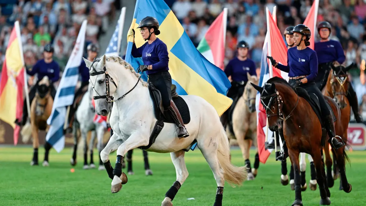 Reit-WM Aachen: 11.08.2026, Nordrhein-Westfalen, Aachen: Pferdesport, Weltmeisterschaft, Eröffnungsfeier. Reiter mit Fahnen der teilnehmenden Länder reiten durch den Parcours. Foto: Uwe Anspach/dpa +++ dpa-Bildfunk +++