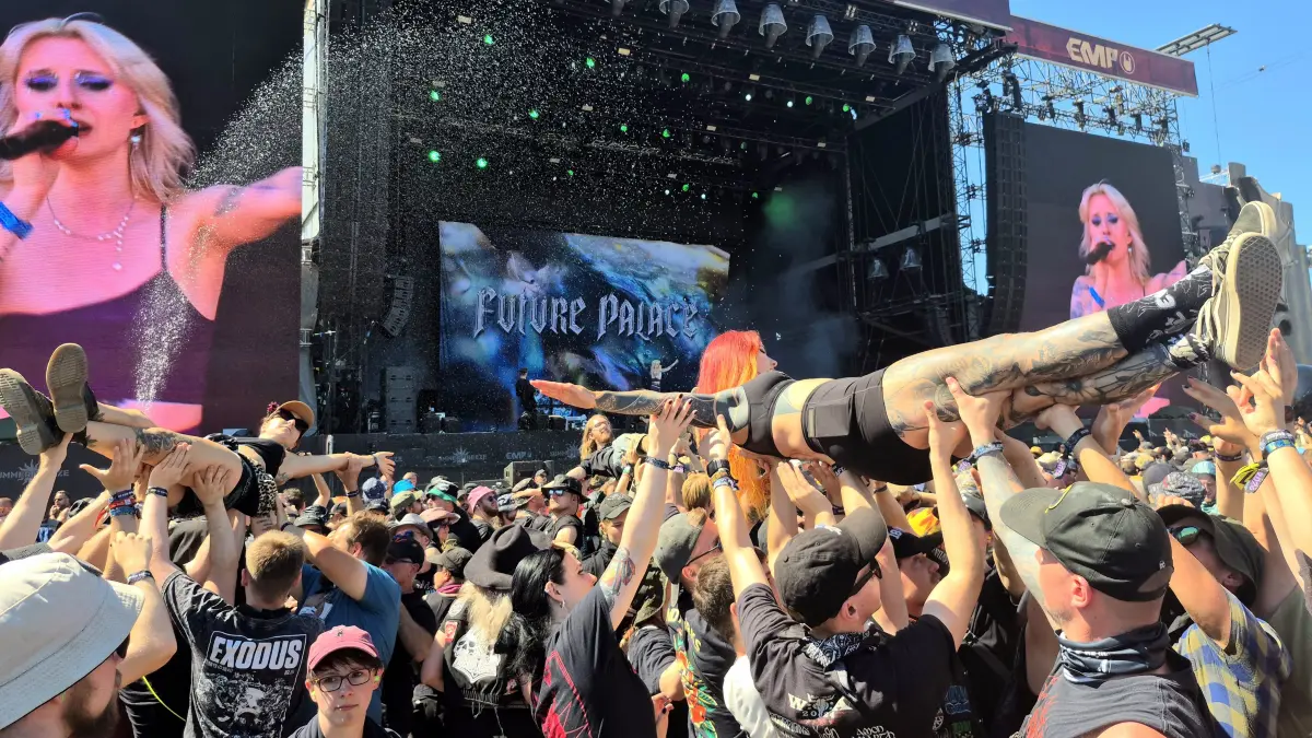 Gleich drei crowdsurfende Metal-Fans werden hier in Richtung Bühne getragen. Währenddessen legt Future Palace einen eindrucksvollen Auftritt in der Mittagshitze hin. Wasserfontänen kühlen die Zuschauenden ab. (Summer Breeze)