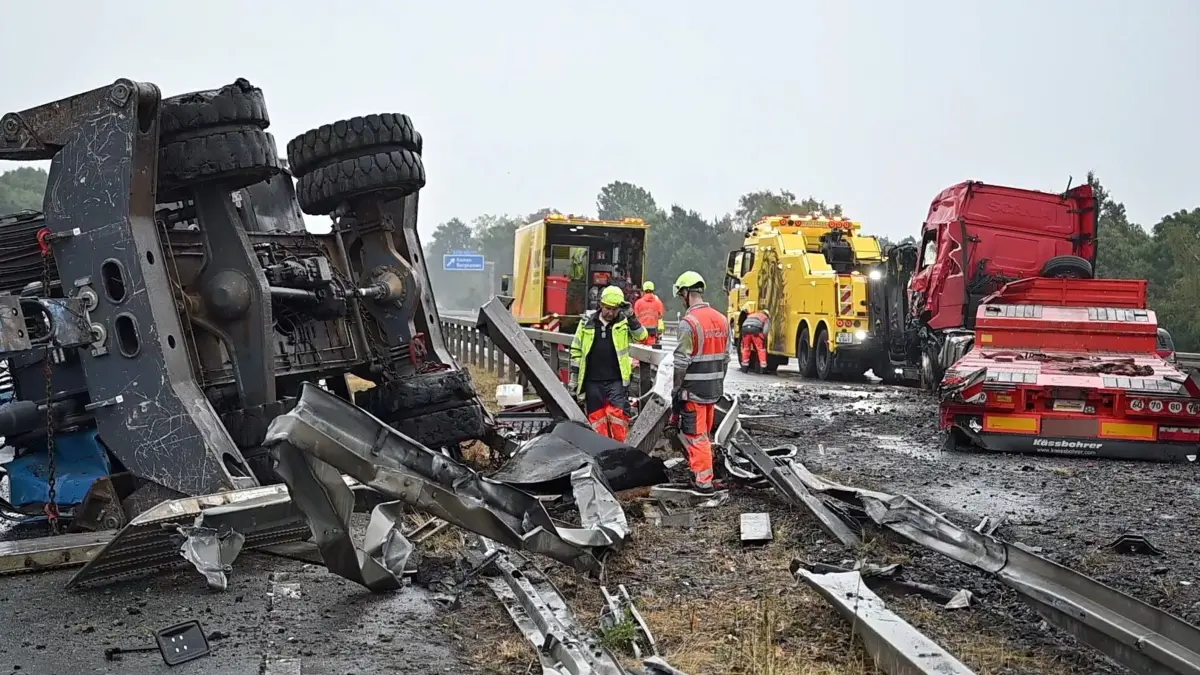 Schwertransporter mit Baukran umgekippt: 18.08.2026, Nordrhein-Westfalen, Kamen: Ein umgekippter Schwertransporter (r) und dessen Ladung, ein Baukran (l), liegen quer über den Mittelstreifen der Autobahn A2 und blockieren die Autobahn in Richtung Hannover und Oberhausen. Die Aufräum- und Bergungsarbeiten gestalten sich schwierig. Foto: Bernd Thissen/dpa +++ dpa-Bildfunk +++