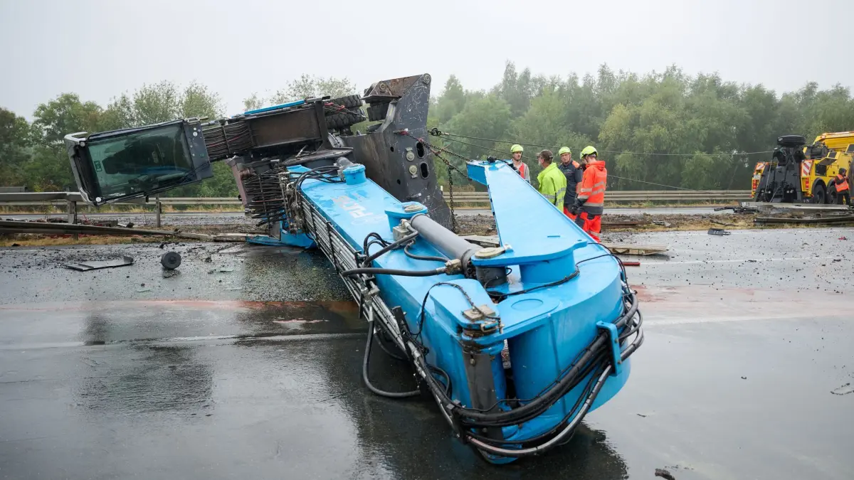 Schwertransporter mit Baukran umgekippt: 18.08.2026, Nordrhein-Westfalen, Kamen: Mitarbeiter einer Bergungsfirma bereiten das Aufrichten eines umgekippten Baukrans mit Stahlseilen vor, der nach einem Unfall quer über dem Mittelstreifen der Autobahn A2 liegt, nachdem er bei dem Unfall von einem Schwerlasttransporter gerutscht war. Die Autobahn in Richtung Hannover und Oberhausen ist dadurch blockiert. Foto: Bernd Thissen/dpa +++ dpa-Bildfunk +++