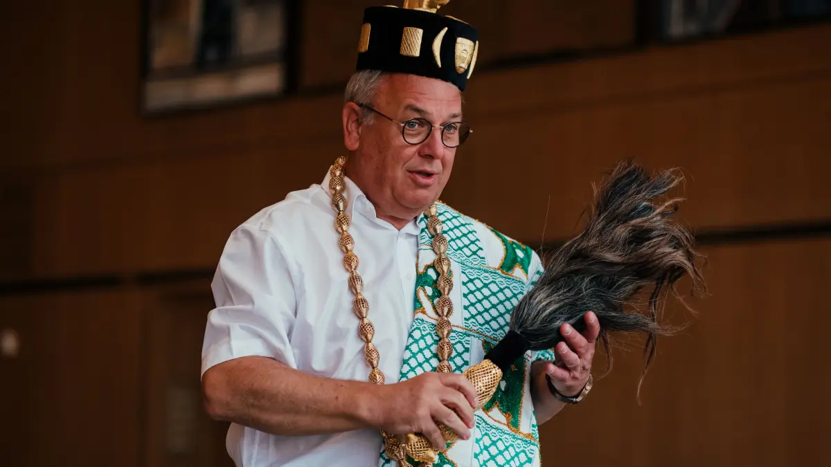 Reutlingens Oberbürgermeister Thomas Keck zeigt die traditionellen Insignien aus Bouaké: Kopfbedeckung, Halskette, Stoff und Fliegenwedel stehen für Würde, Autorität und Gastfreundschaft.