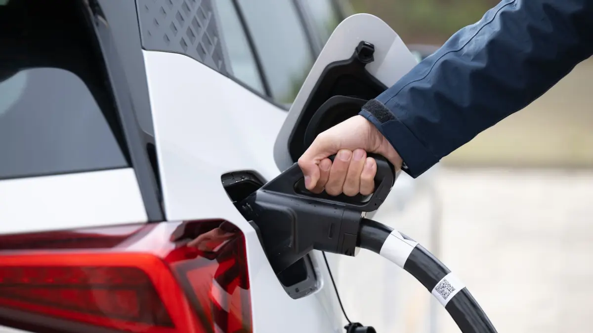 Ein Mann steckt ein Ladekabel in ein Elektroauto: ARCHIV - Schnellladen kostet: Öffentliches DC-Laden kann zwar effizienter sein, ist aber meist teurer als Haushaltsstrom. (zu dpa: «Wie lade ich mein E-Auto am besten?») Foto: Sebastian Kahnert/dpa/dpa-tmn - Honorarfrei nur für Bezieher des dpa-Themendienstes +++ dpa-Themendienst +++