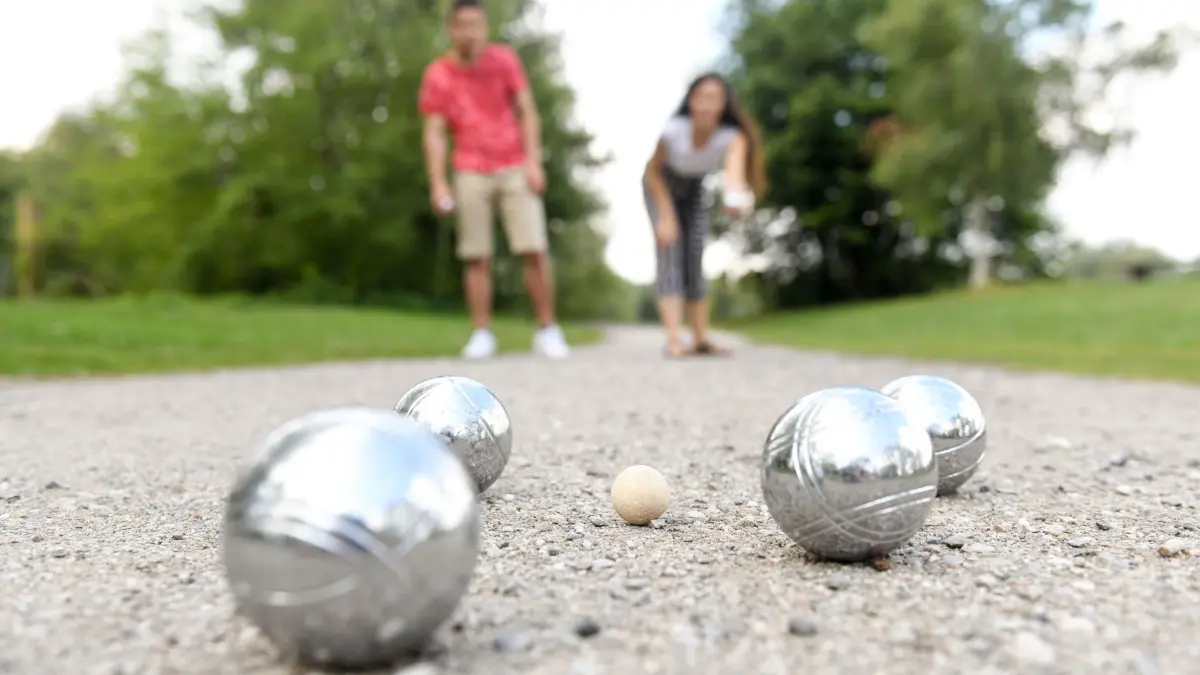 Ein Paar spielt Boule im Park: ILLUSTRATION - Feinmotorik, Konzentration und Lebensfreude: Boule spielen ist gut für Körper und Geist. Mit ein paar Tipps wird's nicht zur einseitigen Belastung. (zu dpa: «Was Boule spielen für die Gesundheit bringt») Foto: Tobias Hase/dpa-tmn - Honorarfrei nur für Bezieher des dpa-Themendienstes +++ dpa-Themendienst +++