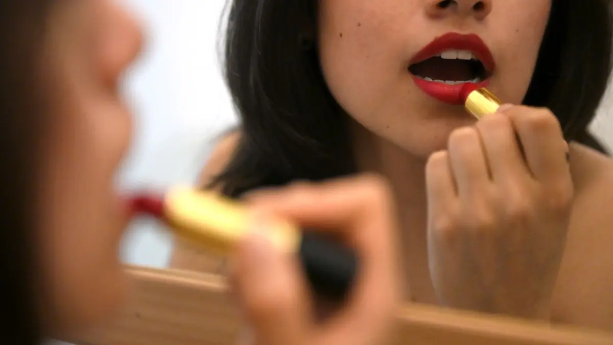 Lippenstift auftragen vor dem Spiegel: PRODUKTION - 10.02.2026, Berlin: Eine junge Frau trägt vor einem Spiegel roten Lippenstift auf. (zu dpa: «Kosmetikbranche steigert Umsatz- Auslandsgeschäft zieht an») Foto: Elisa Schu/dpa +++ dpa-Bildfunk +++