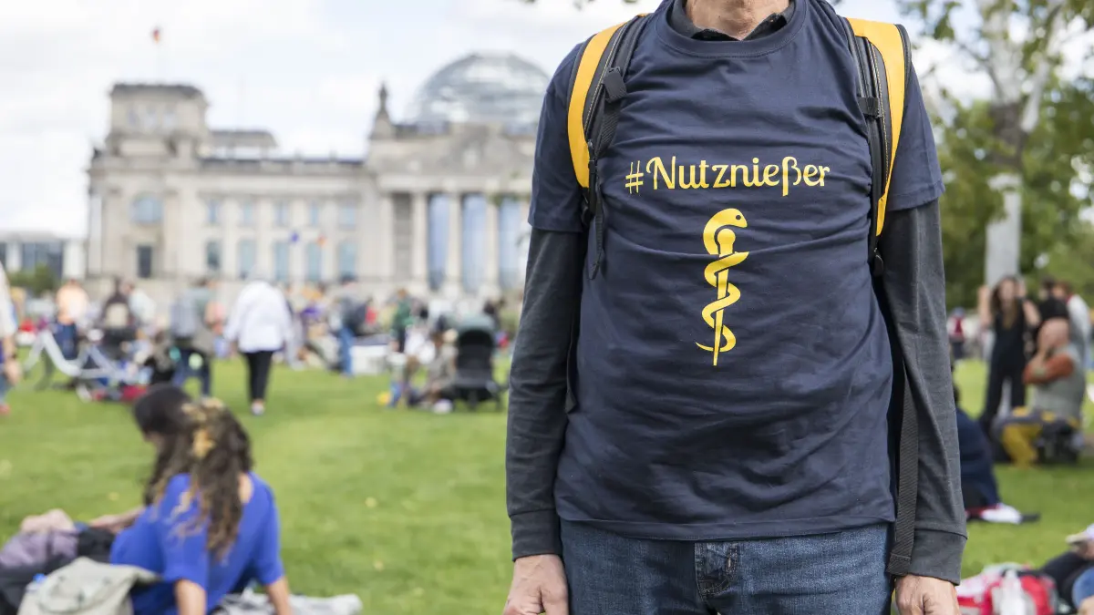 Demonstration Es reicht! Gesundheit statt Sparwahn gegen Sparmaßnahmen im Gesundheitssystem in Berlin : Teilnehmer mit Shirt "#Nutznie§er" bei der Demonstration "Es reicht! Gesundheit statt Sparwahn" gegen Sparma§nahmen im Gesundheitssystem auf dem Platz der Republik zwischen Bundeskanzleramt und Reichstagsgebäude in Berlin am 5. September 2026. Die Versammlung wurde von der Kinderärztin Bea Merscher organisiert nach einem Schlagabtausch mit Bundeskanzler Friedrich Merz.