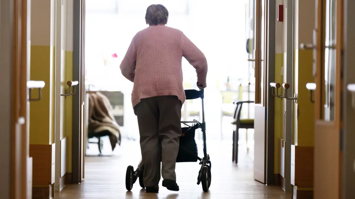 Pflegeheim: ARCHIV - 03.04.2025, Sachsen, Dresden: Eine Frau geht mit einem Rollator in einem Altenheim auf einem Gang entlang. (zu dpa: «13 Senioren im Krankenhaus – Polizei ermittelt im Altenheim») Foto: Sebastian Kahnert/dpa +++ dpa-Bildfunk +++