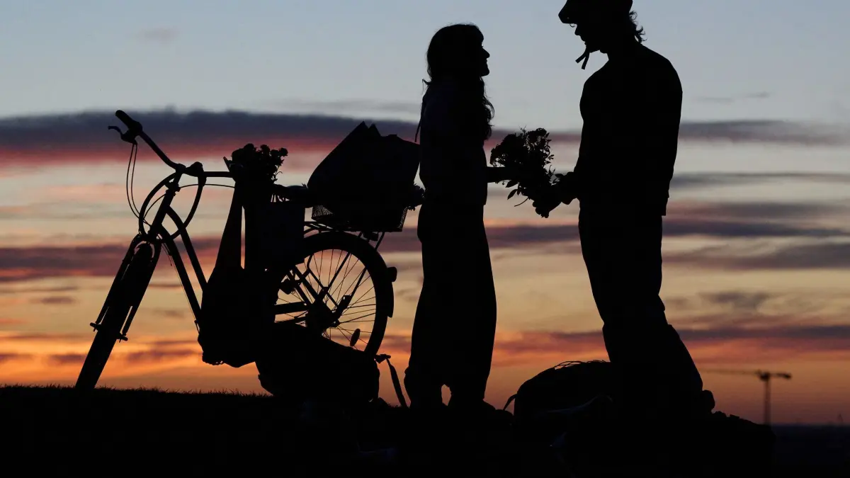 Abendstimmung in München: 23.09.2026, Bayern, München: Ein Mann und eine Frau stehen mit einem Blumenstrauß im Olympiapark und schauen sich den Sonnenuntergang an. Foto: Sven Hoppe/dpa +++ dpa-Bildfunk +++