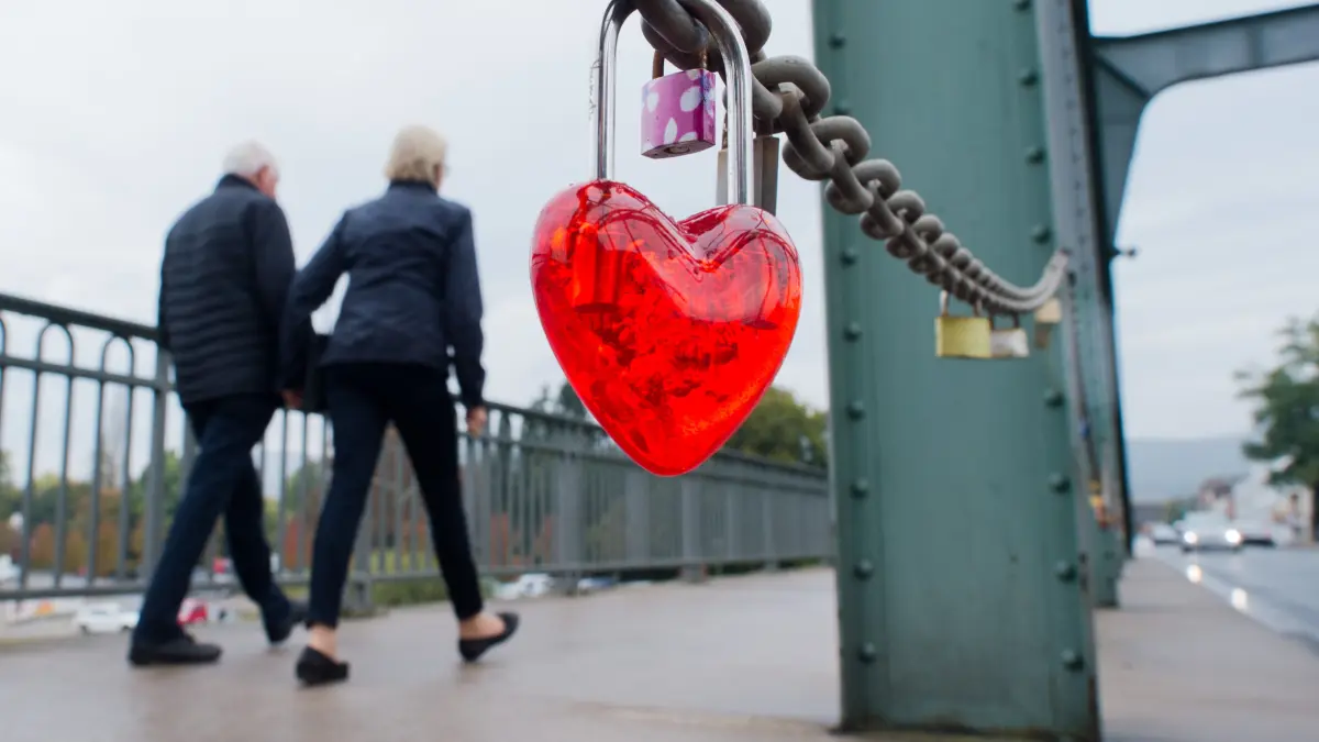 Ein Paar geht am 13.10.2014 über die Hindenburgbrücke in Rinteln im Landkreis Schaumburg (Niedersachsen) an "Liebesschlössern" vorbei. Zum Zeichen ihrer Liebe haben viele Paare Schlösser an der Brücke befestigt. Foto: Julian Stratenschulte/dpa ++ +++ dpa-Bildfunk +++