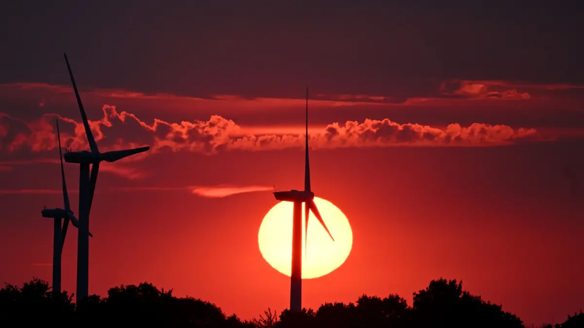 Sonnenuntergang in Nordrhein-Westfalen: ARCHIV - 15.08.2026, Nordrhein-Westfalen, Erp: Hinter Windrädern färbt die sinkende Sonne den Himmel rot. (zu dpa: «Studie: Europas Firmen für mehr Investitionen in Erneuerbare») Foto: Federico Gambarini/dpa +++ dpa-Bildfunk +++