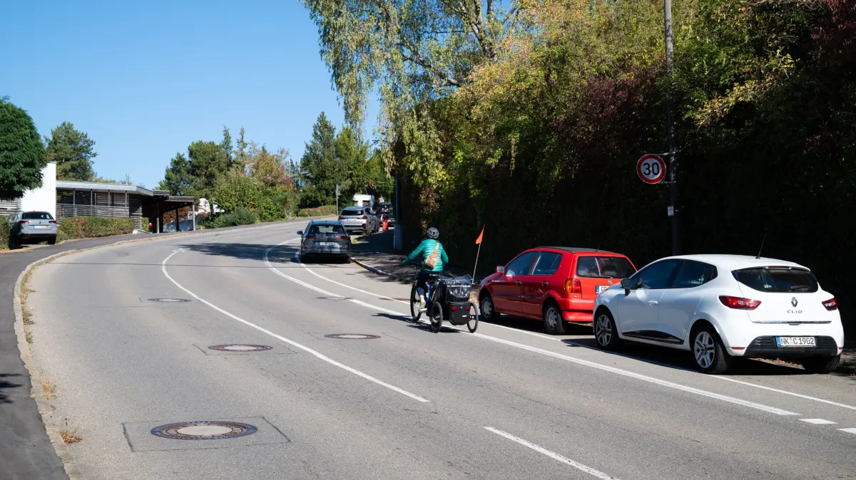 Waldhäuser Straße mit parkenden Autos und Radfahrerin. Hier der Abschnitt zwischen der Bäckerei Gehr an der Haltestelle Robert-Gradmann-Weg und dem Abzweig zur Eduard-Spranger-Straße.