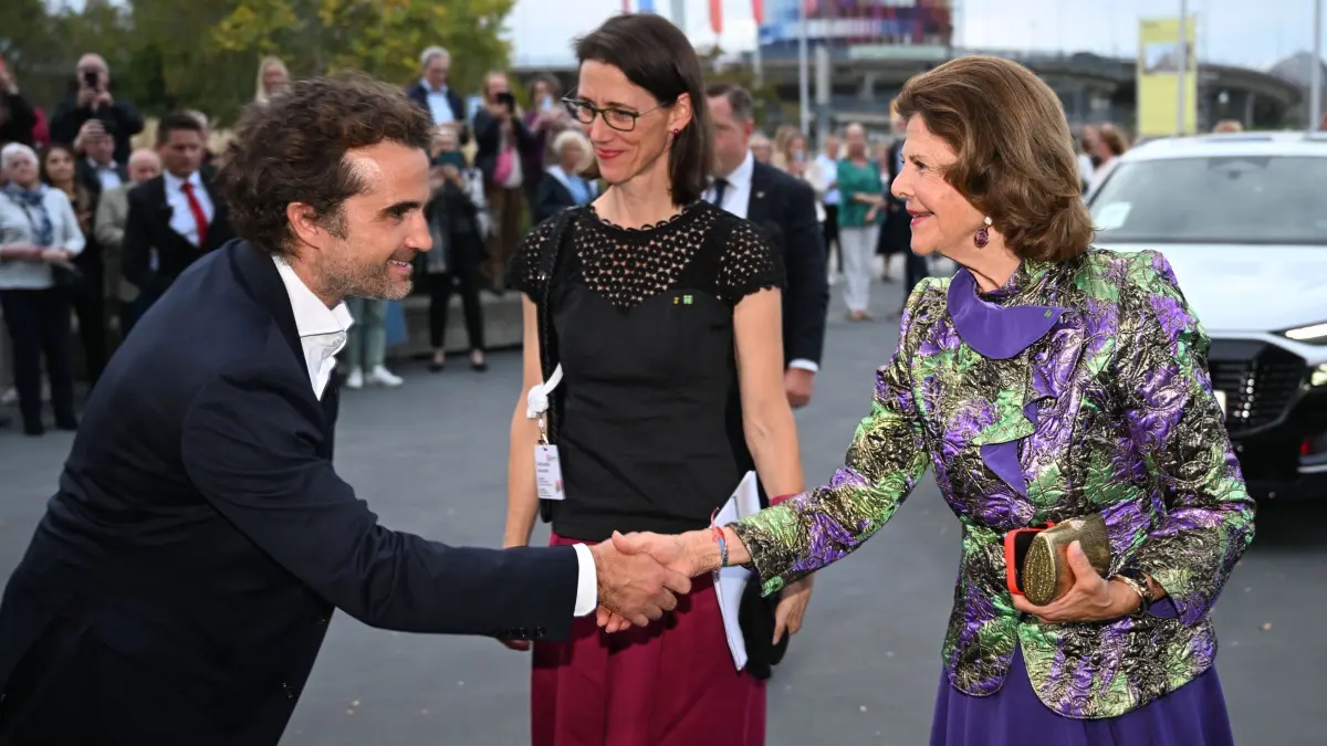 Königin Silvia kommt zum Jubiläum der Mentor-Stiftung: 07.10.2026, Baden-Württemberg, Konstanz: Schauspieler Oliver Wnuk (l) begrüßt Königin Silvia von Schweden (r), während Bettina Bernadotte in der Mitte steht. Schwedens Königin nimmt anlässlich des zehnjährigen Bestehens der Mentor-Stiftung Deutschland an den Feierlichkeiten in Konstanz und auf der Insel Mainau teil. Den Auftakt bildet das Bühnenprojekt «wir_jetzt_hier» im Bodenseeforum Konstanz. Foto: Felix Kästle/dpa +++ dpa-Bildfunk +++