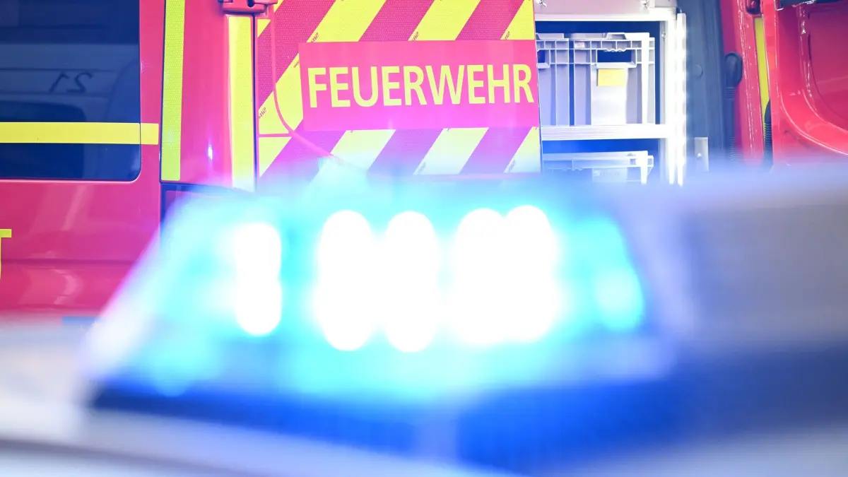 Feuerwehr Symbolbild: Ein Fahrzeug der Feuerwehr steht bei einem Einsatz auf einer Straße, während im Vordergrund das Blaulicht eines Polizeifahrzeugs zu sehen ist. (zu dpa: «Anhänger voller Weinflaschen brennt - B38a gesperrt»)