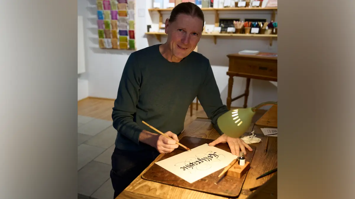 Matthias Gröschke sitzt an einem Tisch und schreibt das Wort „Kalligraphie“ in Schönschrift.