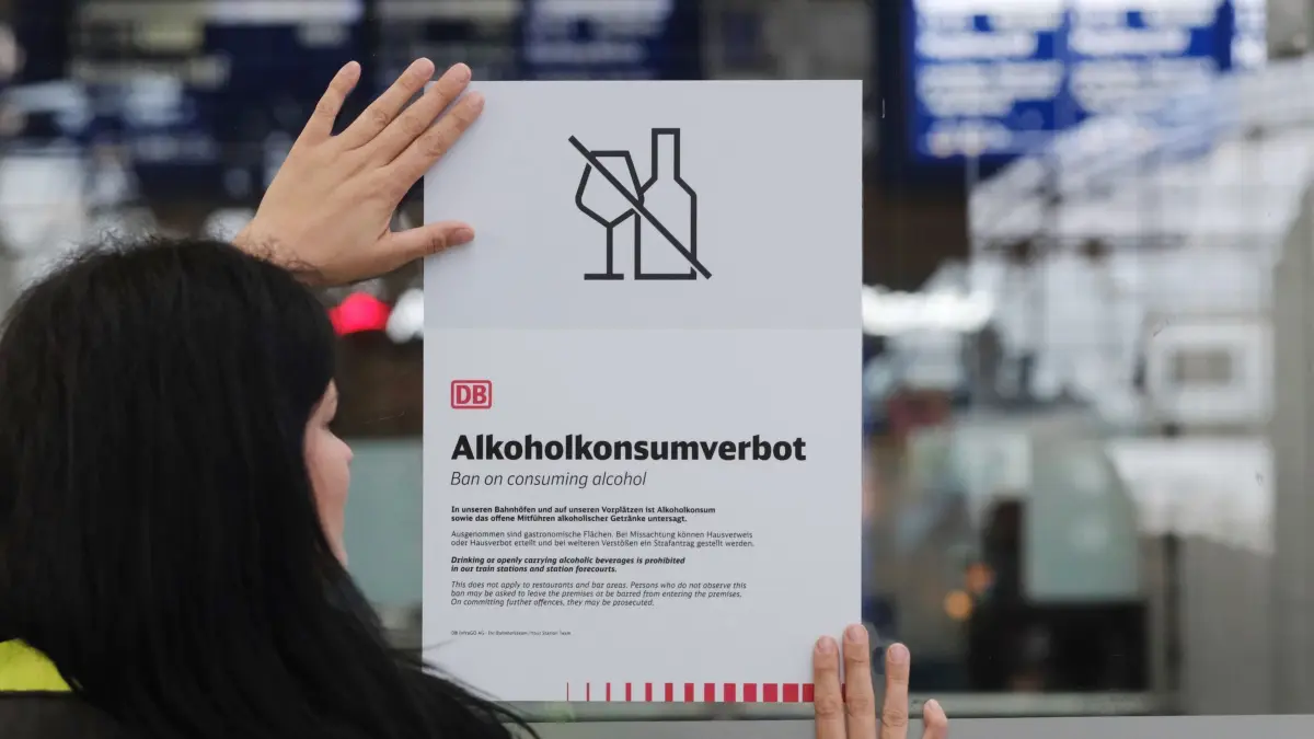Alkoholverbot an Bahnhöfen: Eine Mitarbeiterin des Sicherheitsdienstes der Deutschen Bahn hält im Hauptbahnhof ein Plakat mit der Überschrift „Alkoholkonsumverbot“ an eine Glaswand. Die Deutsche Bahn untersagt ab dem 15. Oktober 2026 den Konsum von Alkohol an all ihren Bahnhöfen. (zu dpa: «Alkoholverbot an Bahnhöfen - Das Wichtigste im Überblick»)
