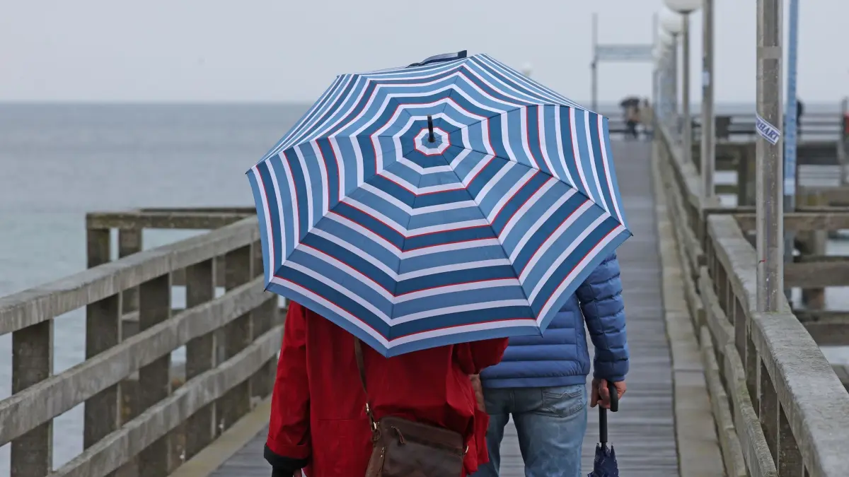 Regenwetter an der Ostsee: Mit Regenschirm und wetterfester Bekleidung sind Spaziergänger auf der Seebrücke an der Ostsee unterwegs. Kaltes und regnerisches Wetter dominiert im Norden. (zu dpa: «Wo es am Wochenende nass und windig wird»)