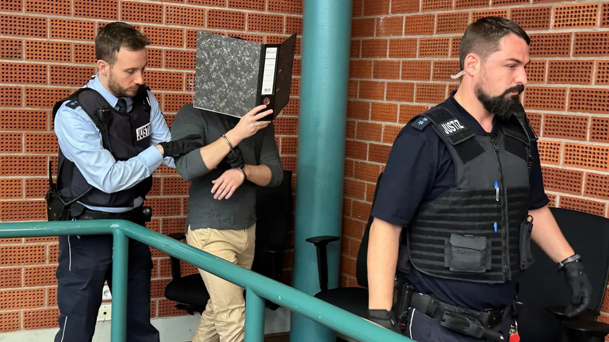 Der falsche Schönheitsarzt wird in Konstanz vor den Richter geführt. Sein Gesicht versteckt er vor den Kameras der Journalisten hinter einem Aktenordner.