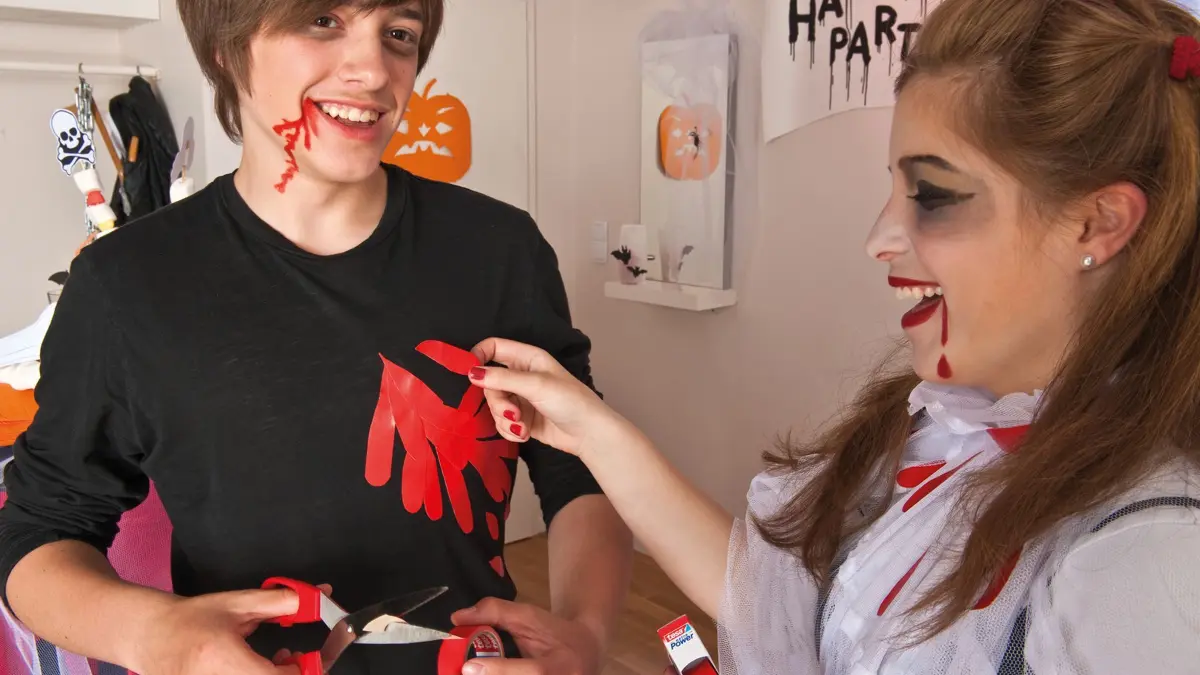 Zwei Kinder verkleiden sich für Halloween: Rotes Gewebeband imitiert Blut: Ausgeschnittene Tropfen und Streifen lassen sich auf ein ausgedientes schwarzes Shirt kleben. (zu dpa: «Drei Last-Minute-Verkleidungsideen für Halloween»)