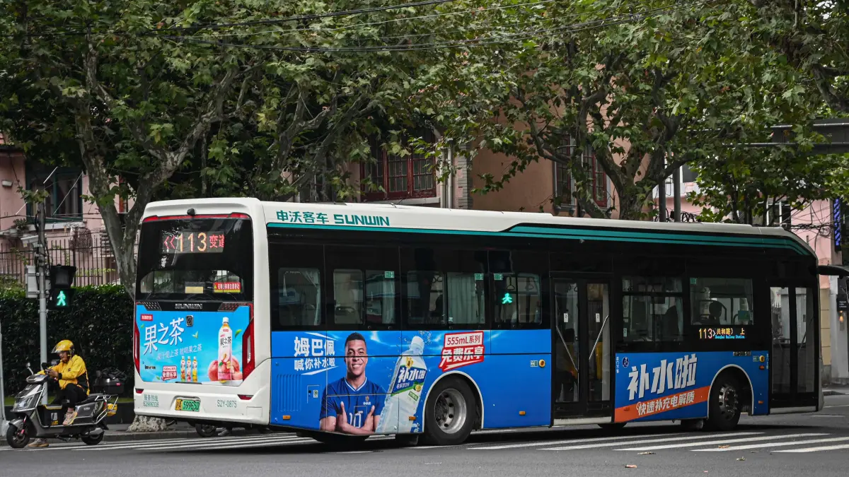 FBL-CHINA-ADVERTISING-MBAPPE: A bus featuring French football star Kylian Mbappe for Dongpeng Beverage Group's "Bushuila" electrolyte drink is seen on a street in Shanghai on October 27, 2026. Kylian Mbappe was dropped on October 27 by two major brands in China after a video circulated online in which the French football star apparently joked about former leader Mao Zedong. (Photo by Jade GAO / AFP)